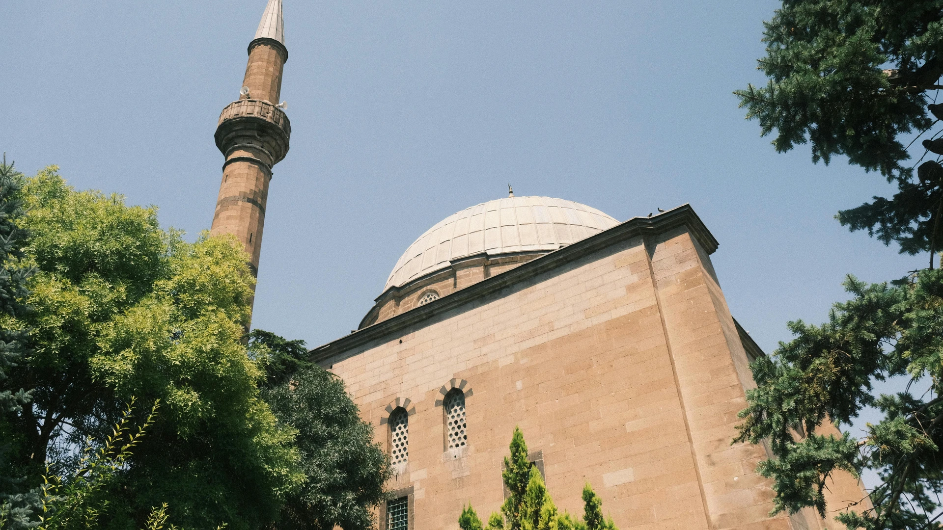 Alexandria, Egypt - Beautiful ottoman mosque in kayseri, türkiye featuring a minaret and dome framed by lush green trees.