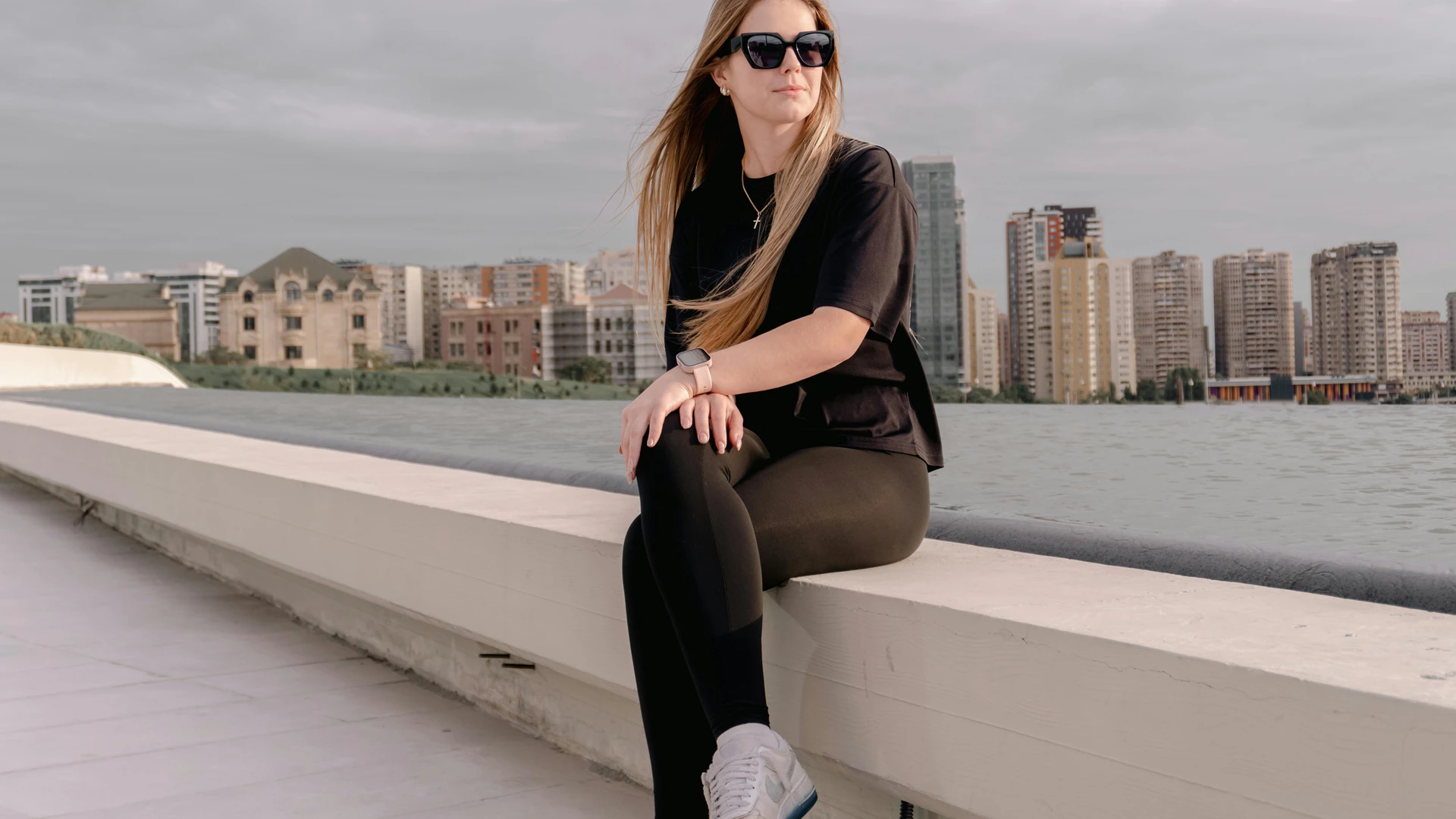 Alexandria, Egypt - Stylish woman sitting by a waterfront with a city skyline in the background. casual and urban scene.