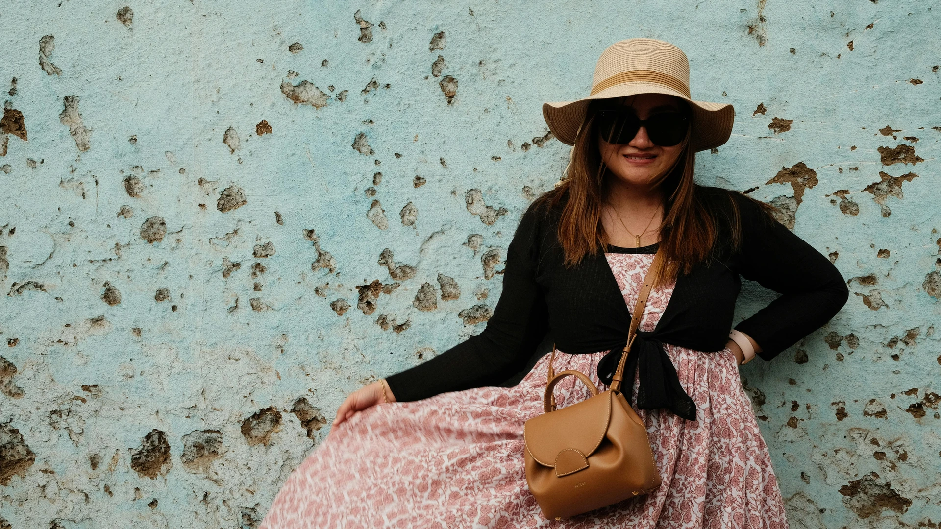 Aswan, Egypt - Fashionable woman in a sunhat stands confidently against a blue weathered wall in aswan, egypt.