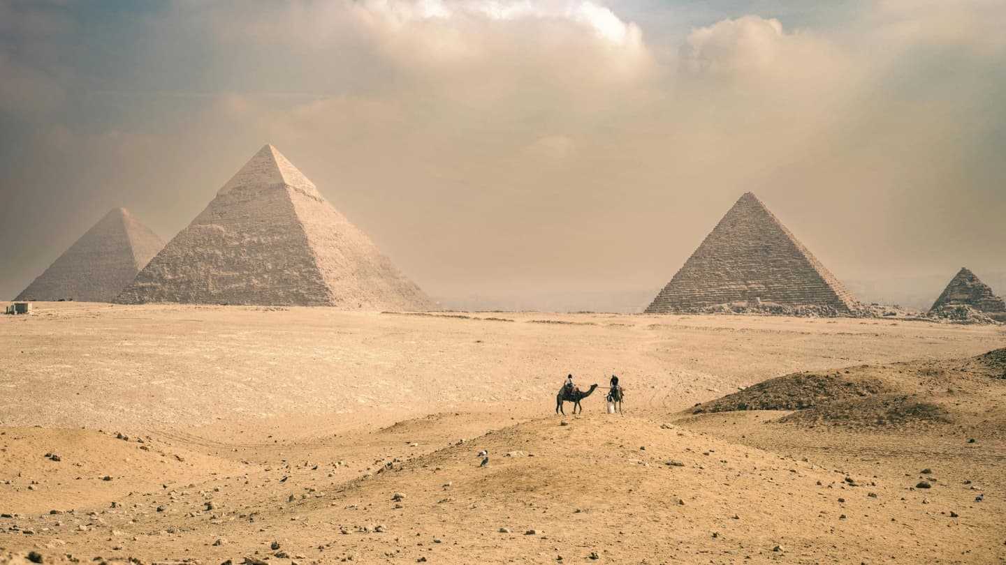 Dahab, Egypt - Explore the majestic pyramids of giza under a sunny sky with distant travelers on camels.