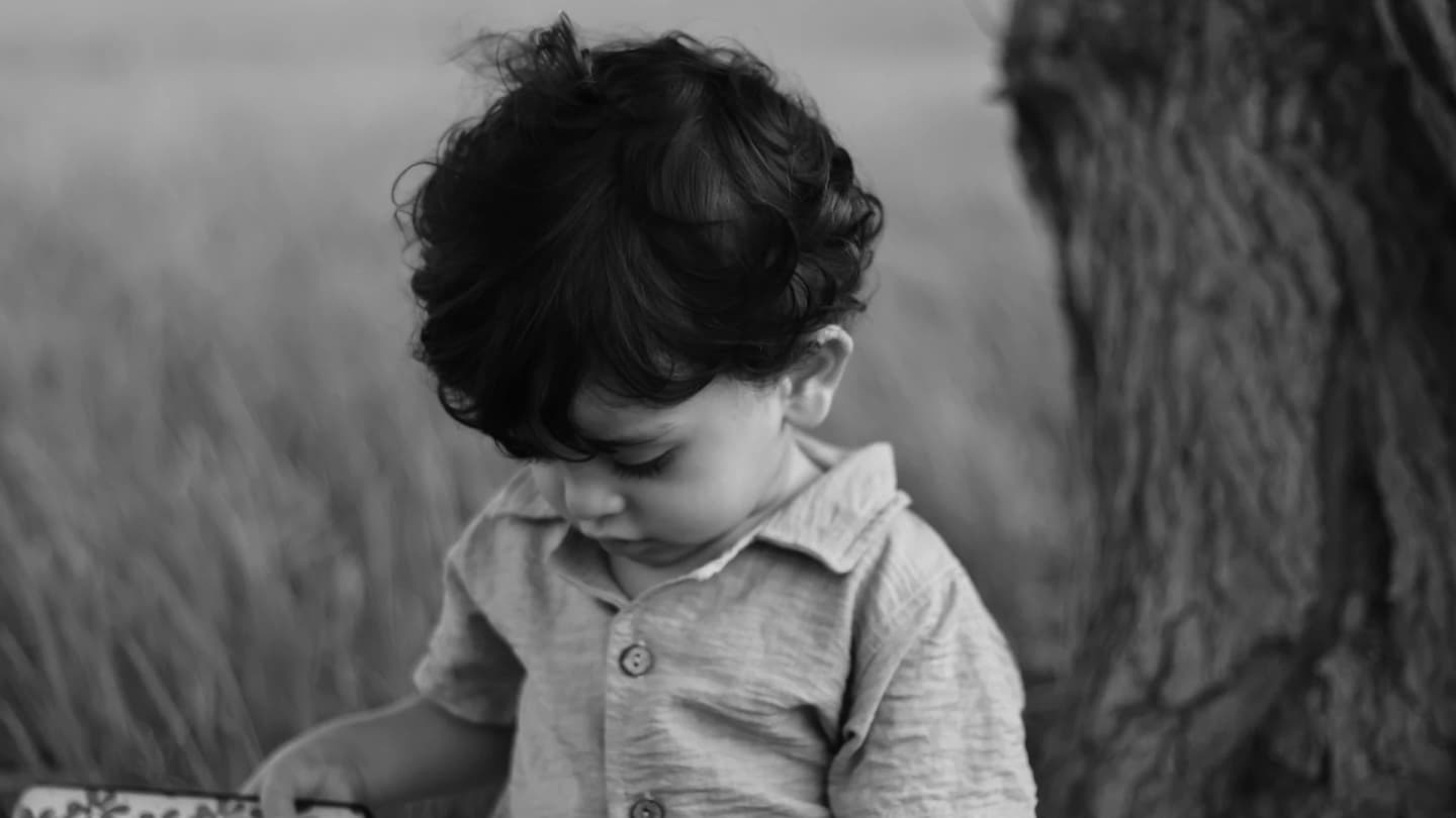 El Gouna, Egypt - Black and white photo of a child standing by a tree, looking down.