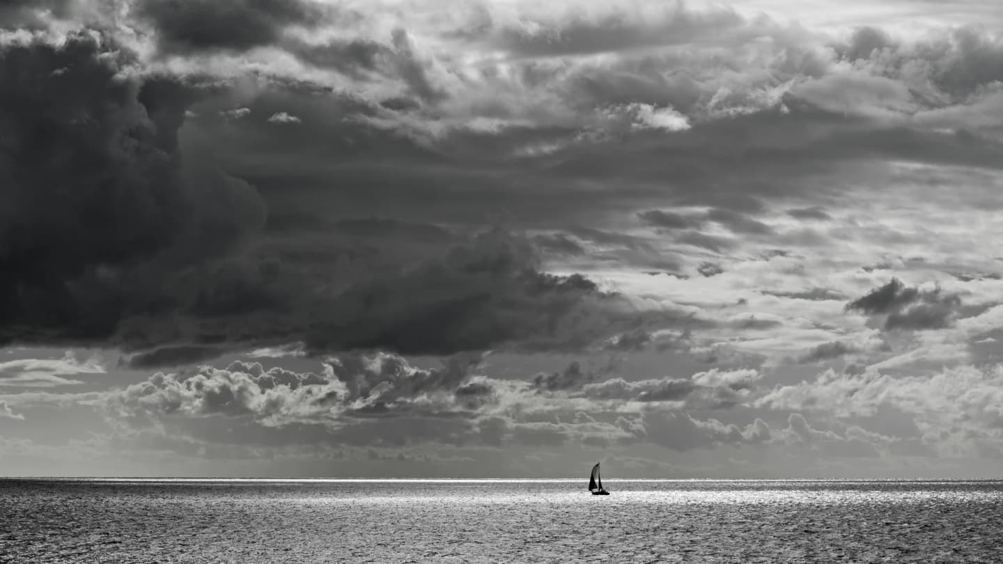 Soma Bay, Egypt - Lone sailboat navigates a vast ocean under dramatic skies in stunning black and white.