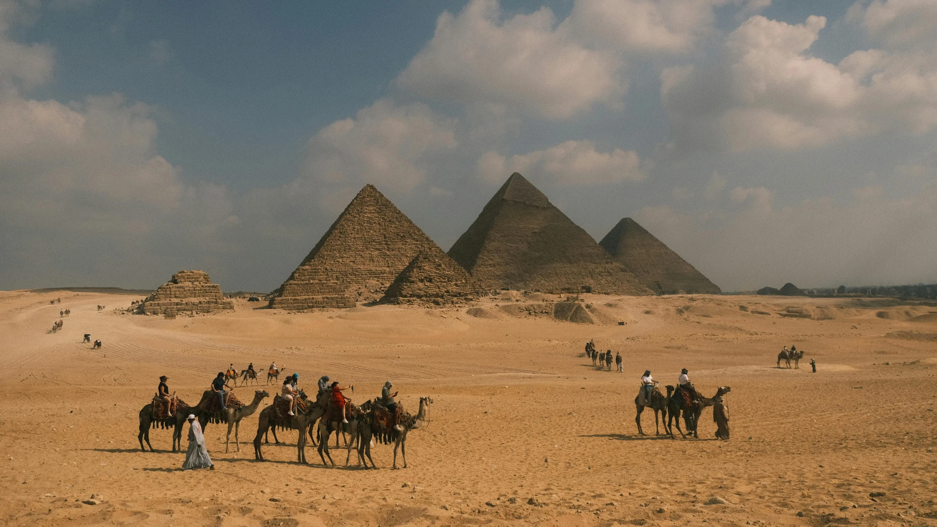 El Alamein, Egypt - Tourists on camel rides near the iconic pyramids of giza under a blue sky.